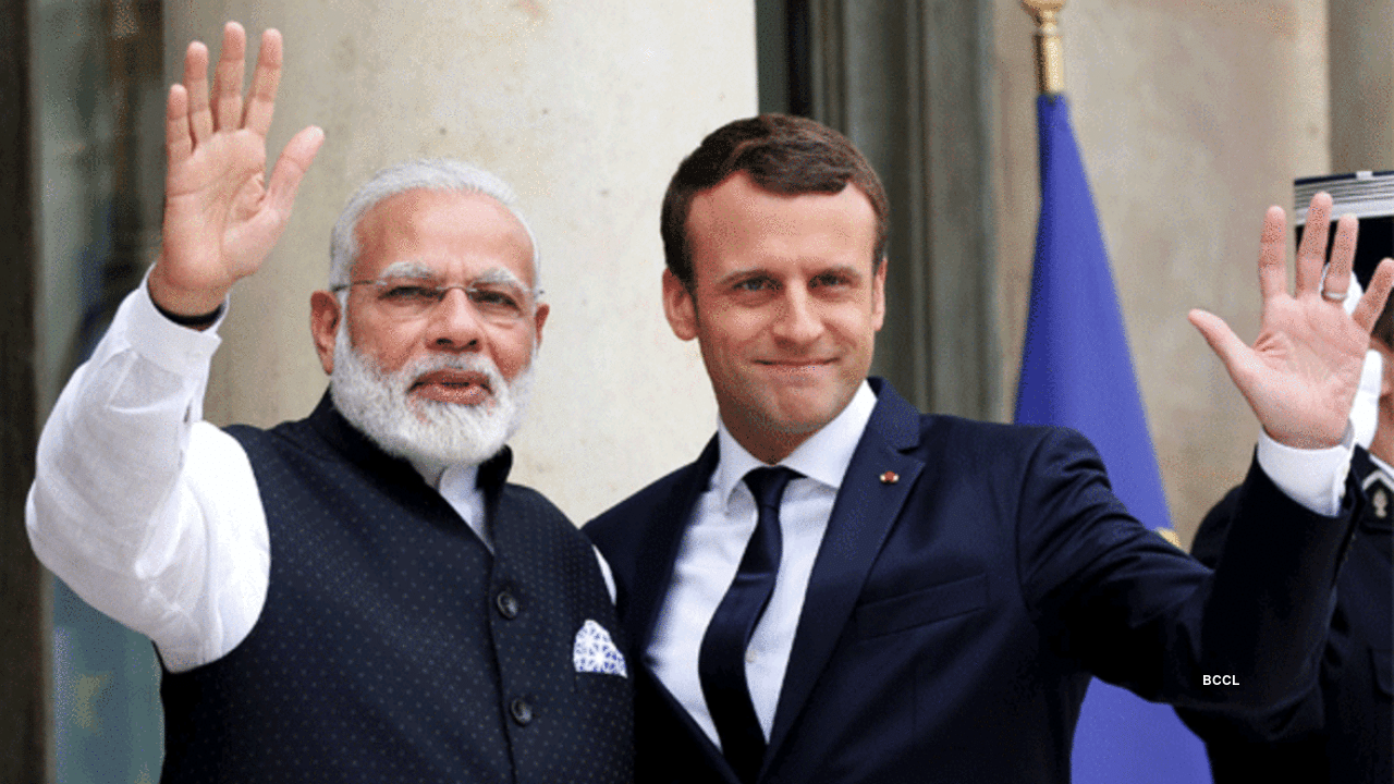 French President Emmanuel Macron and Indian Prime Minister Narendra Modi wave to a crowd.